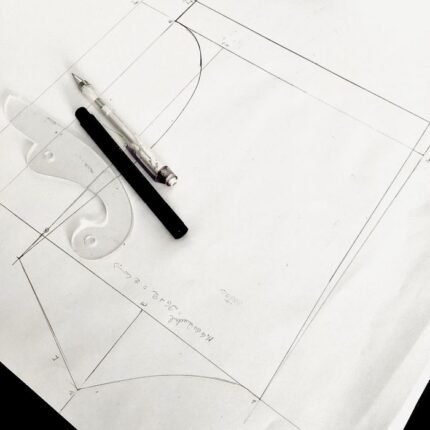 Close-up of a fashion design sketch with drafting tools on a table, highlighting the creative process.